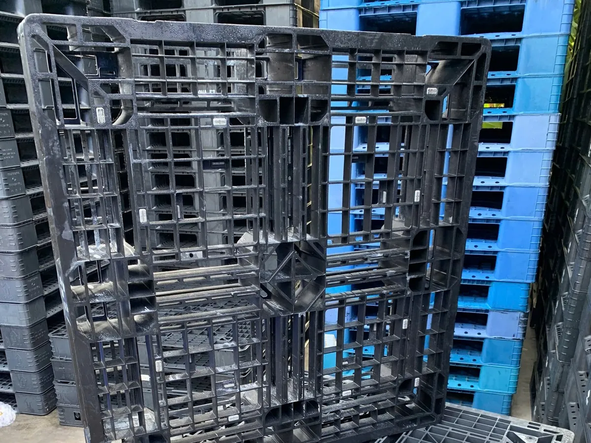 Pallet nhựa cũ mặt lưới 1100x1100x150mm dựng đứng tại kho Mai Trâm, phía sau là các lô pallet cũ xếp chồng